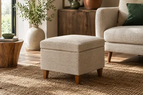 Repose-pieds beige en tissu avec rangement et pieds en bois dans un salon lumineux.