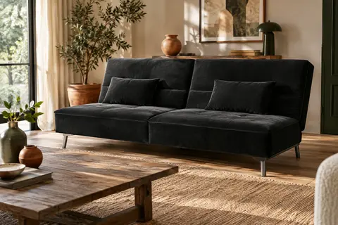 Canapé-lit noir à dossier réglable et petits coussins dans un salon lumineux au décor naturel