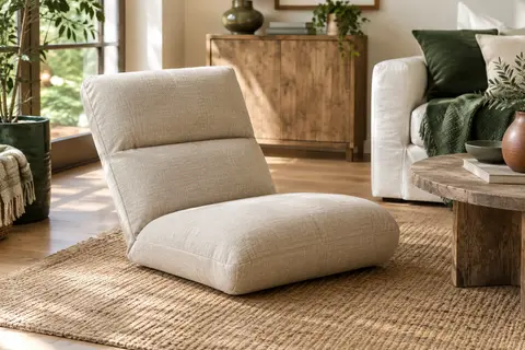 Chauffeuse de sol beige à dossier inclinable, installée dans un salon lumineux près d’un tapis naturel.